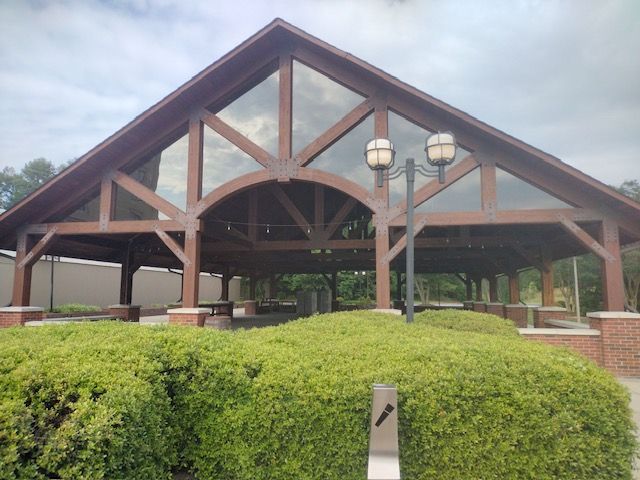 Open-air pavilion with wooden trusses and a green hedge in front