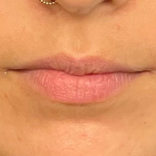 Close-up of a person's lips; pale pink, with a small nose piercing above.