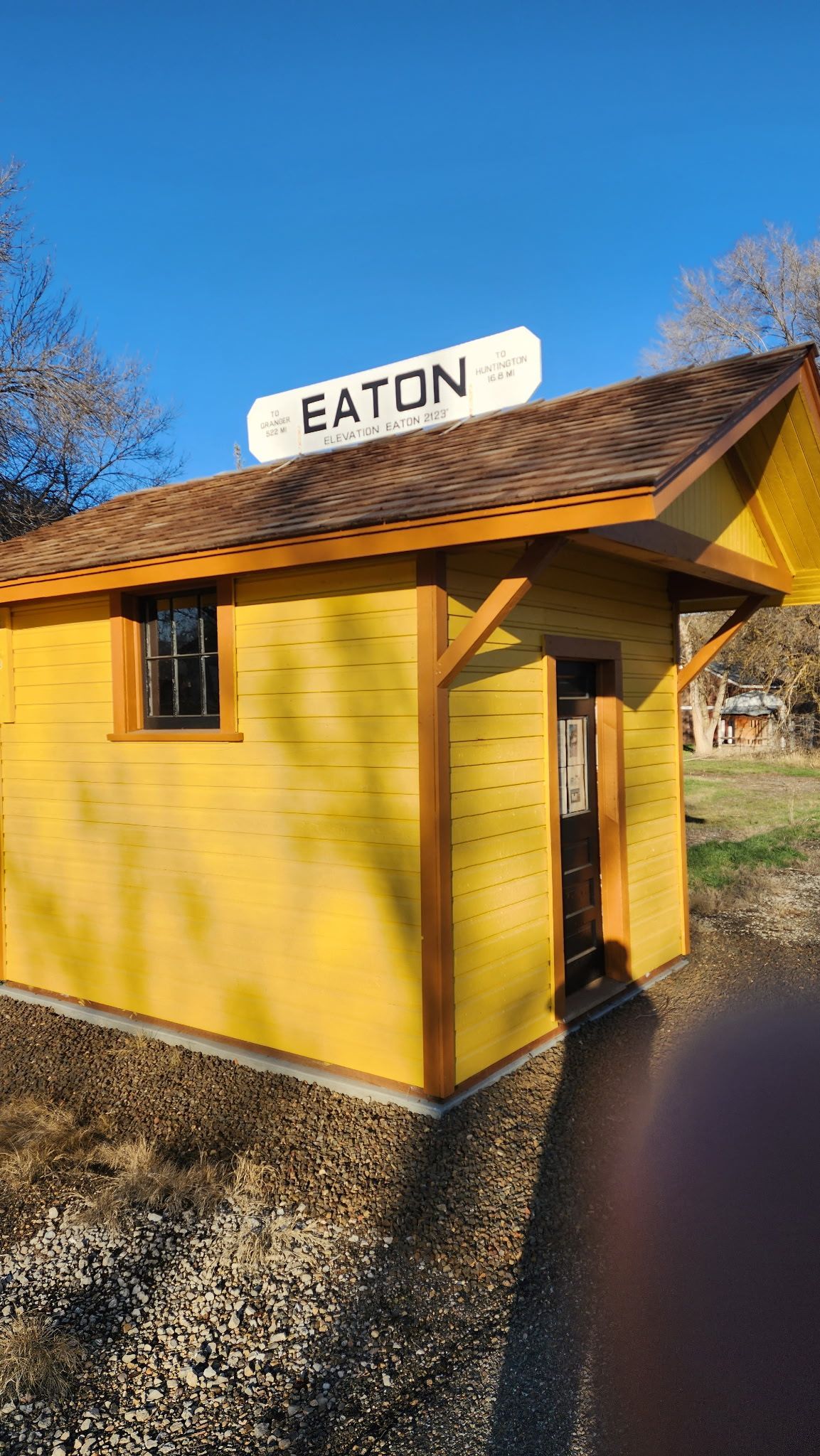 Small yellow building with a sign reading “EATON” on the roof, outdoors in sunlight.