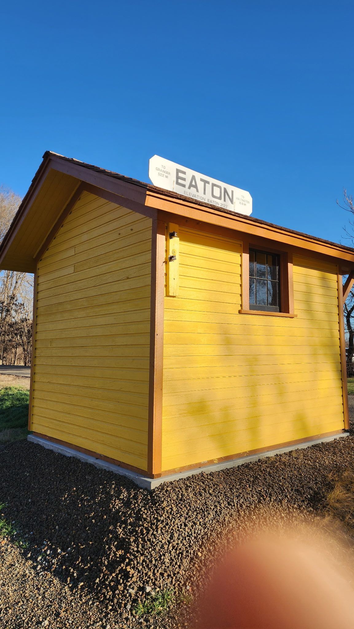 Small yellow shed with brown trim and a white “Eaton” sign under a blue sky.