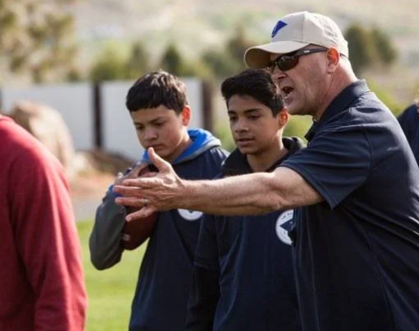Coach gesturing to two boys during an outdoor sports practice