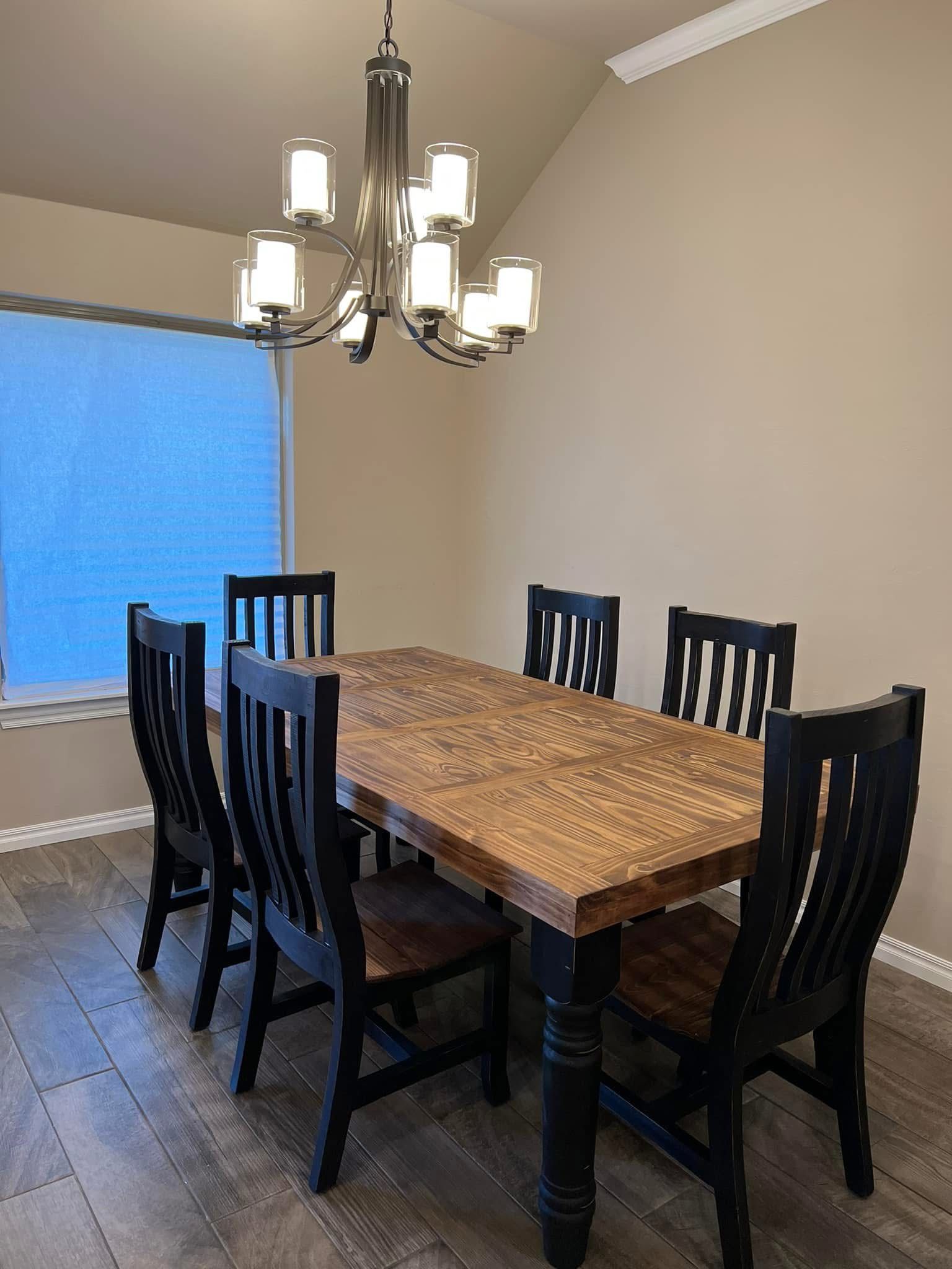 Dining room with wooden table and six black chairs, under a chandelier.