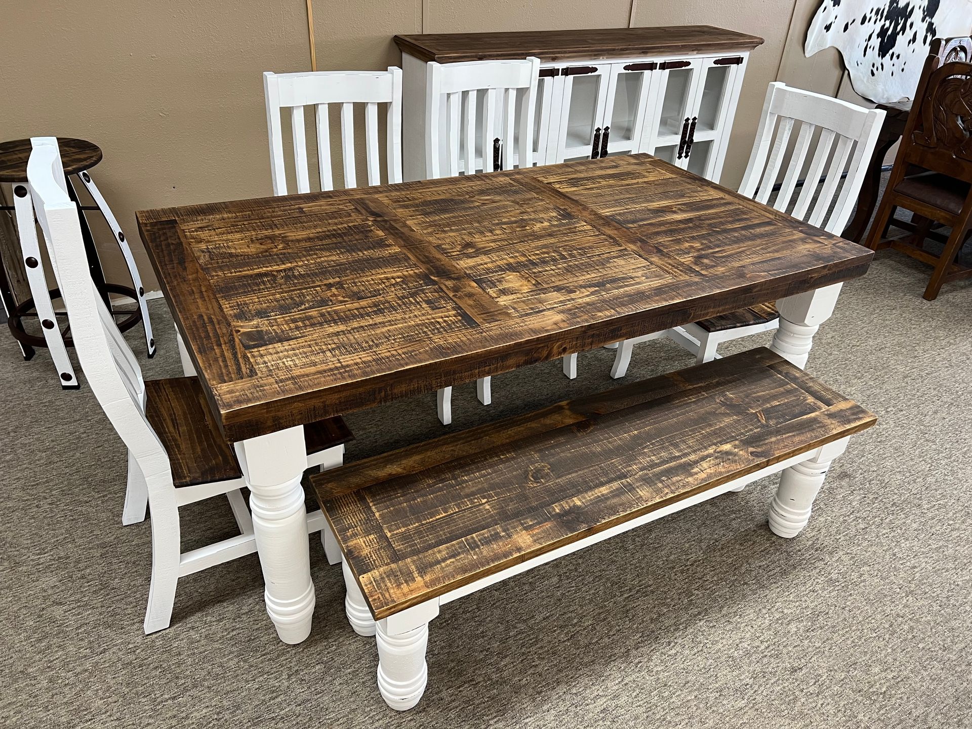 Rustic dining set with a wood table, bench, and chairs, and a white cabinet in a showroom.