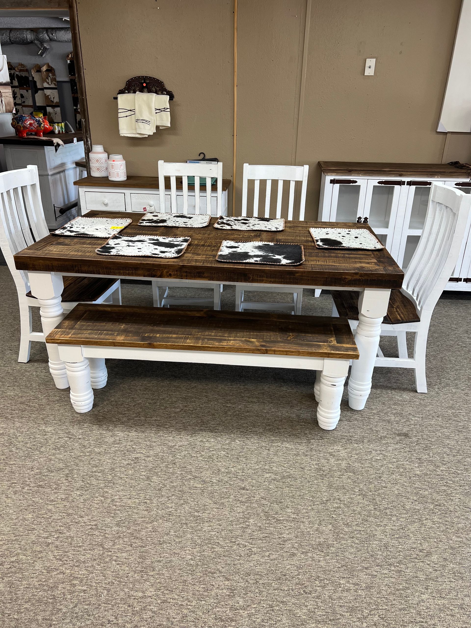 Rustic dining set with a wood table, bench, and chairs, and a white cabinet in a showroom.