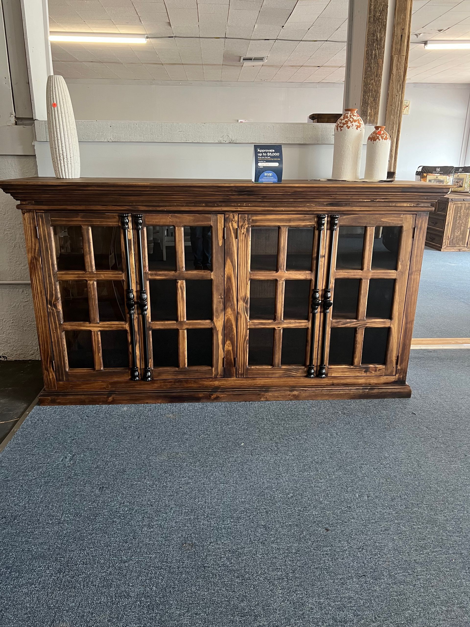 Wooden cabinet with glass doors, dark brown finish, sitting on blue carpet, items on top.