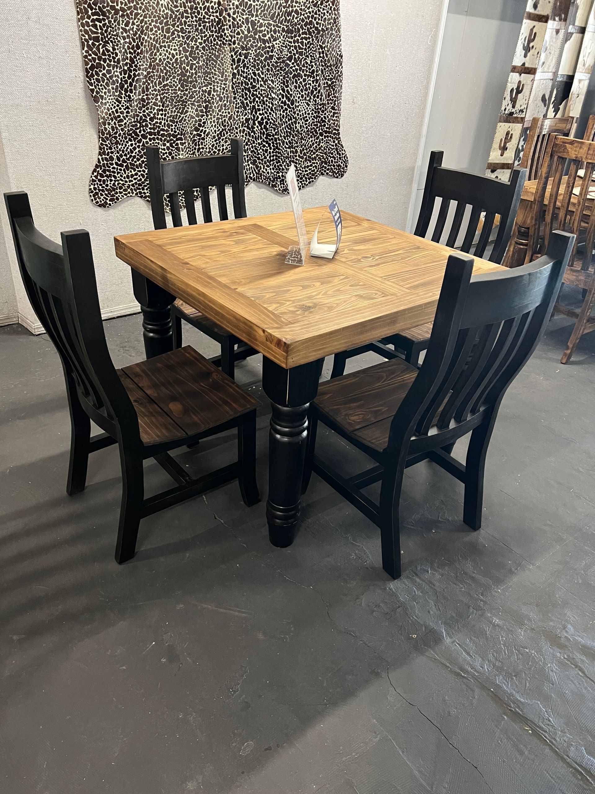 A square wooden dining table with four matching chairs sits by a window with blinds in a room.
