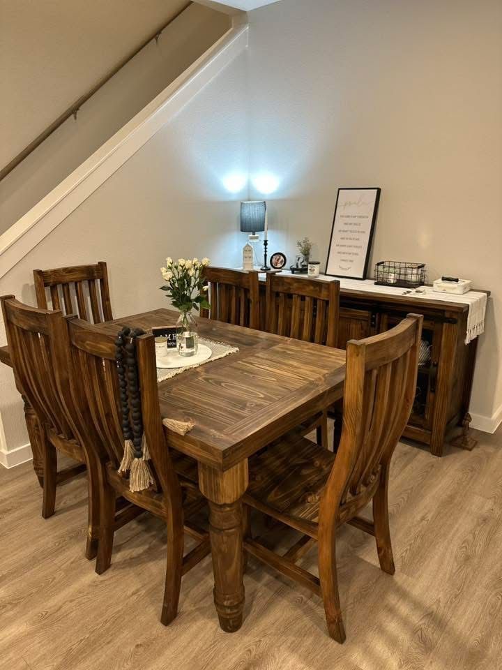 Wooden dining set in a well-lit room with a buffet and stairs in the background.