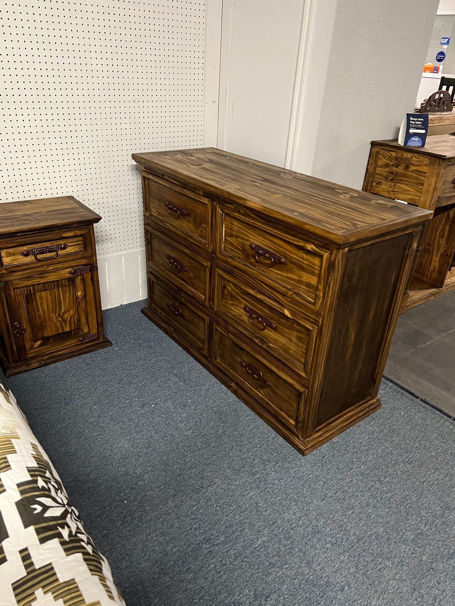 Rustic bedroom set with a wooden bed, nightstand, and dresser. Cow-themed artwork on the wall.