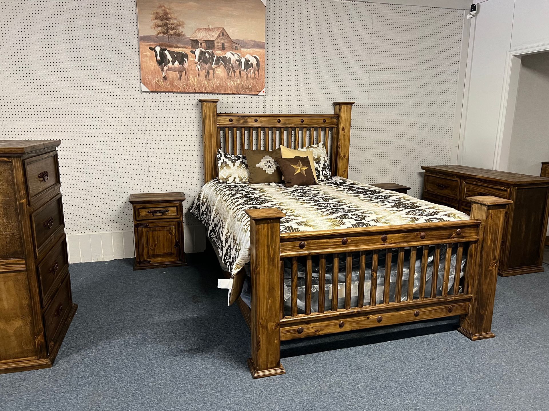 Rustic bedroom set with a wooden bed, nightstand, and dresser. Cow-themed artwork on the wall.