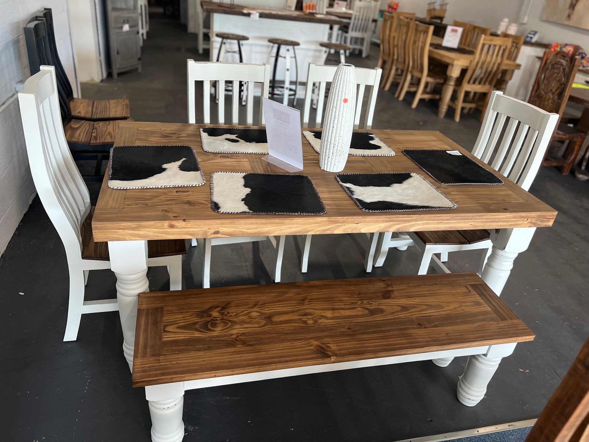 Wooden dining table with bench and white chairs, black and white placemats.