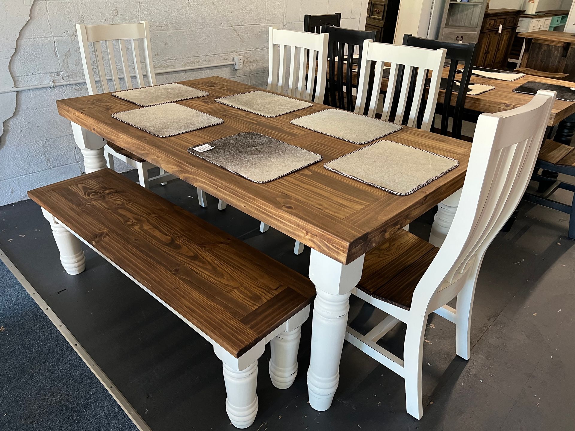 Wooden dining table with bench and white chairs, black and white placemats.