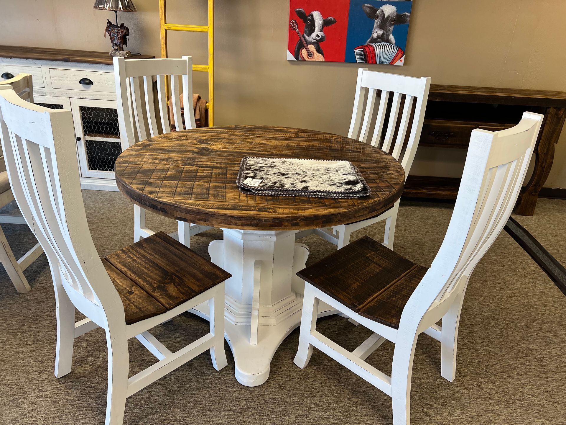 A round dining table with four white chairs and teacups, set in a store with wood furniture.