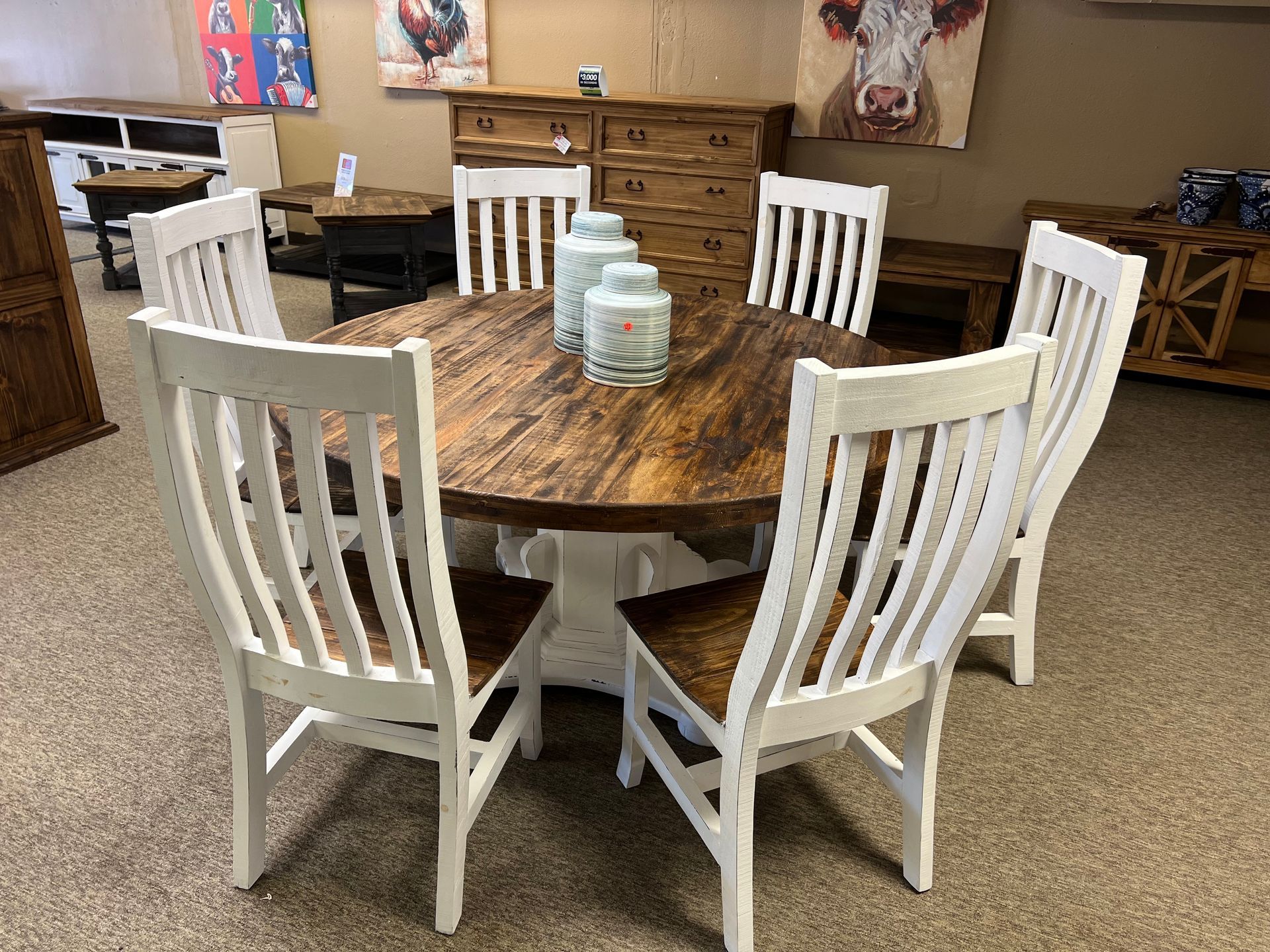 Dining table with six white chairs, brown tabletop, and a white base, in a furniture store.