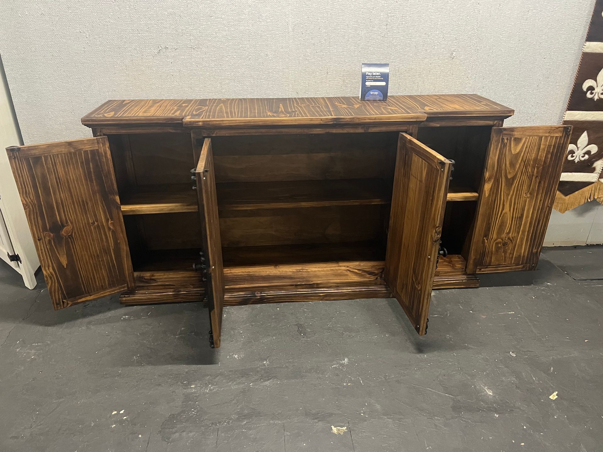 Wooden cabinet with dark, rustic design, featuring X-patterned doors. In a warehouse setting.