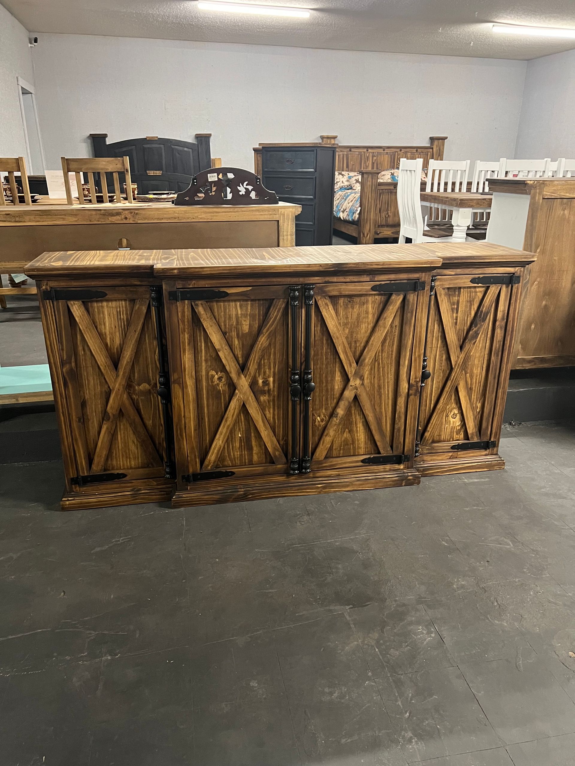 Wooden cabinet with dark, rustic design, featuring X-patterned doors. In a warehouse setting.