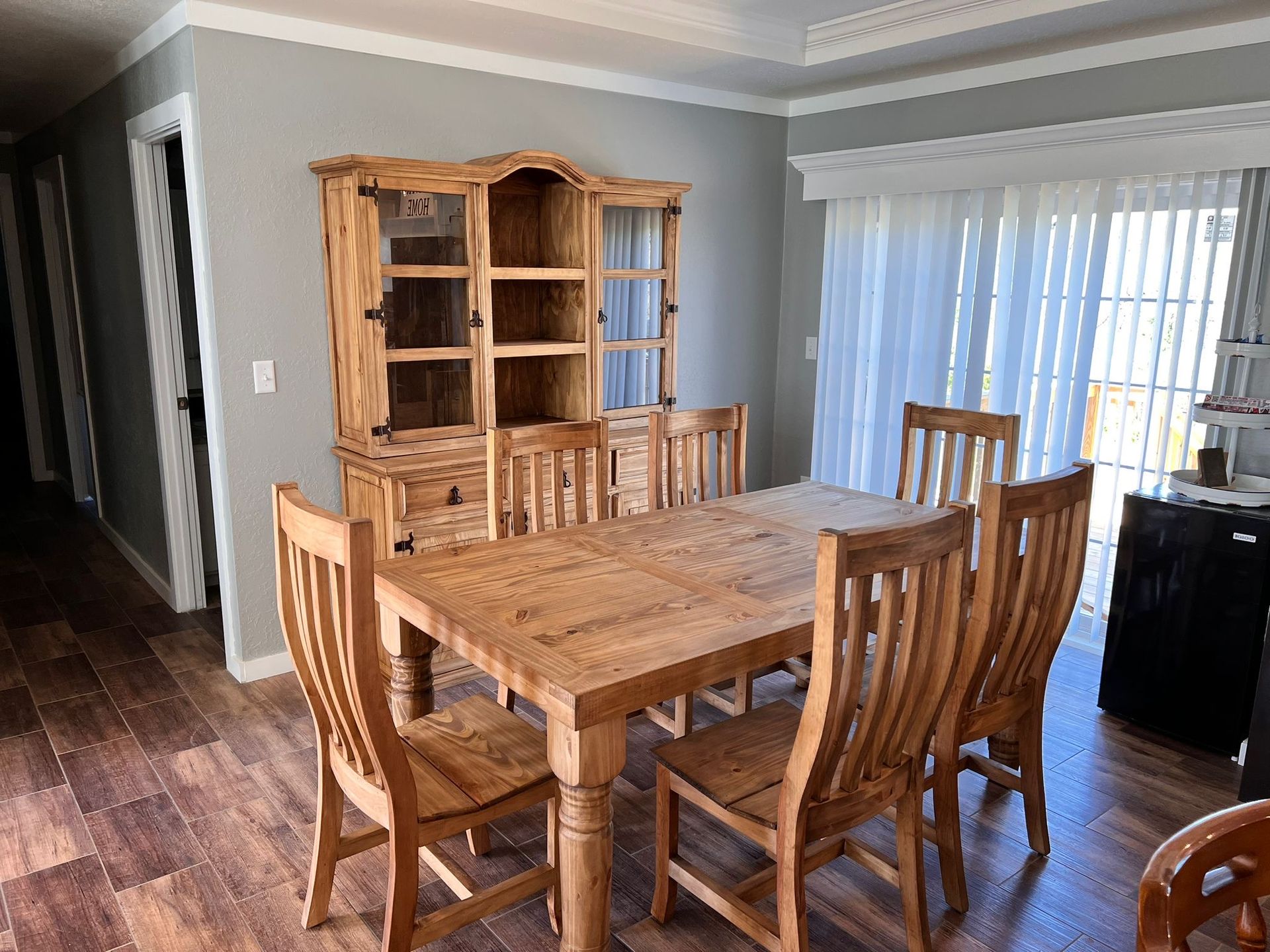 Dining room with wooden table, chairs, hutch, and sliding glass door.