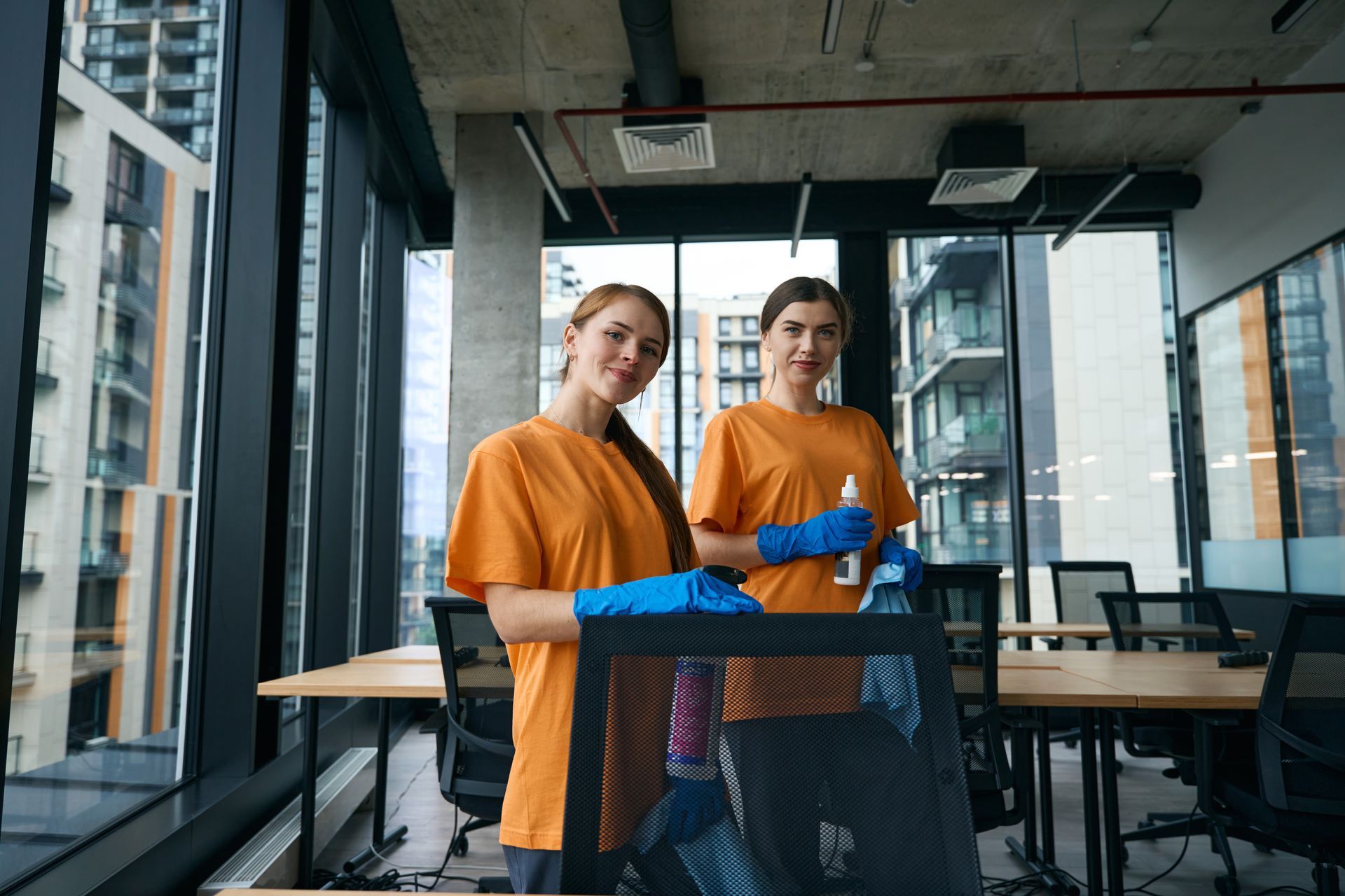 Two people in orange shirts and blue gloves standing behind a table in a modern office space.