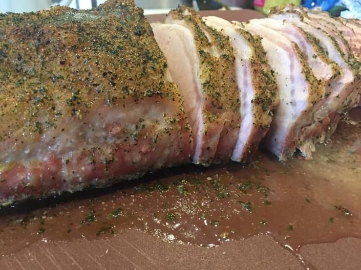 Sliced seasoned roast meat on a wooden cutting board with juices pooling around it