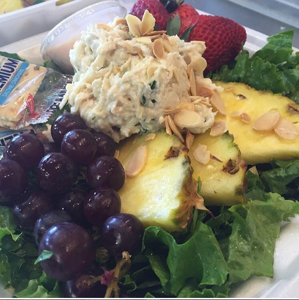 Salad plate with grapes, strawberries, pineapple, lettuce, and a scoop of chicken salad topped with almonds