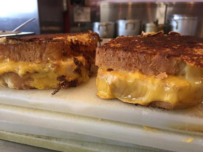 Grilled cheese sandwich halves on a white cutting board, golden brown and oozing melted cheese.