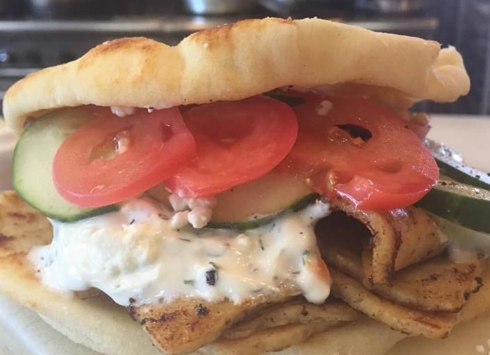 Close-up of a pita sandwich with tomato, cucumber, and creamy sauce on a plate
