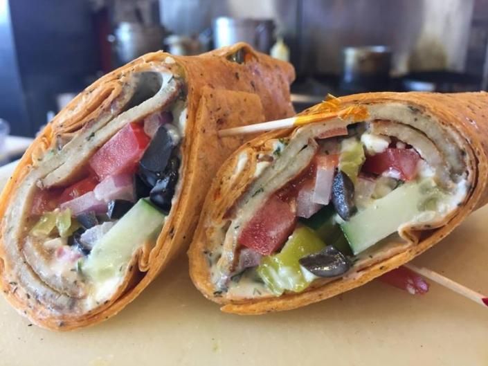 Cut wrap sandwich halves with tomato, lettuce, olives, and creamy filling on a wooden board
