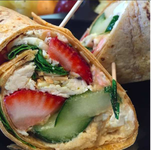 Close-up of a wrap cut open, showing strawberries, cucumber, chicken, and greens inside.