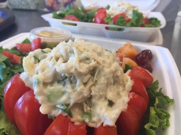 Salad topped with creamy tuna or chicken salad, served on a white foam plate with tomatoes and greens
