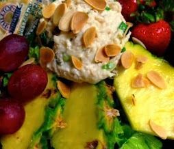 Colorful fruit dessert with whipped cream and sliced almonds, surrounded by strawberries, grapes, and kiwi