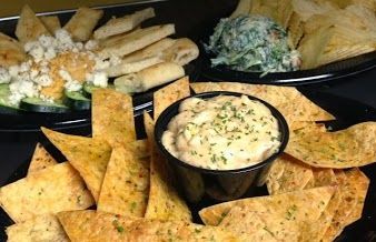 Assorted tortilla chips with creamy dip and guacamole in black bowls on a dark platter