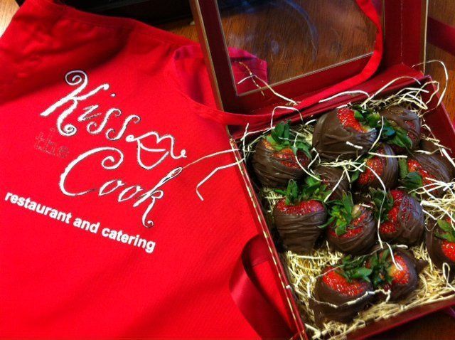 Red Kiss Cook catering shirt beside a box of chocolate-covered strawberries with decorative drizzle