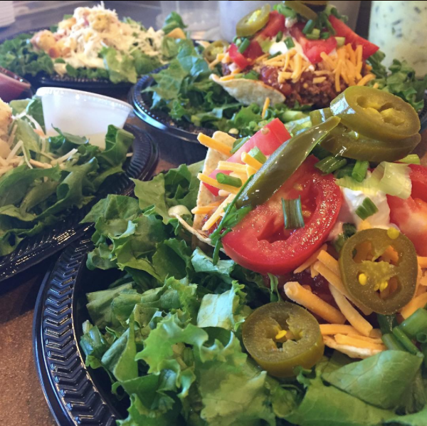 Salad bar with leafy greens, sliced jalapeños, tomatoes, shredded cheese, and assorted toppings