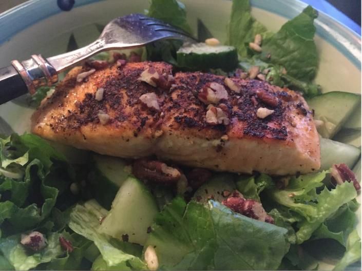 Grilled fish fillet on a green salad with cucumber slices and a spoon on the plate