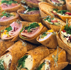 Tray of rolled tortilla wraps with ham, greens, and cheese, arranged in rows