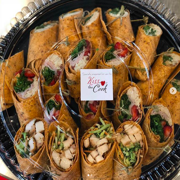 Assorted wrap sandwiches in a black tray with a “Kiss the Cook” label.