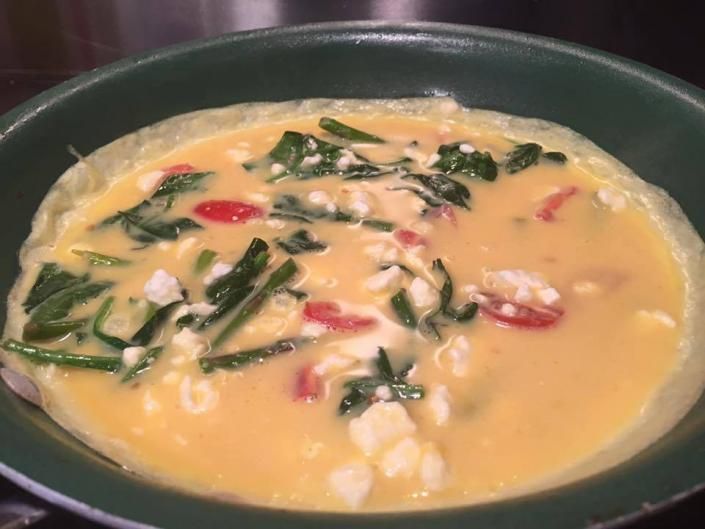 Bowl of creamy orange soup with greens, red pepper slices, and white pieces in a dark bowl
