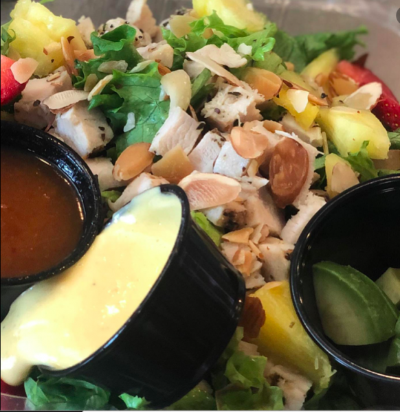 Fresh salad with greens, pineapple, almonds, and two dipping sauces in small black cups
