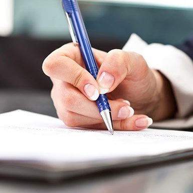 Mano sosteniendo un bolígrafo azul y escribiendo en un bloc de notas blanco.
