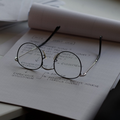 Gafas redondas sobre un cuaderno abierto con un rollo de papel al fondo.