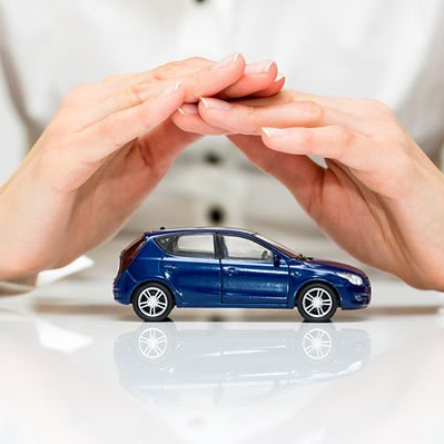 Manos protegiendo un coche de juguete azul sobre una superficie blanca.