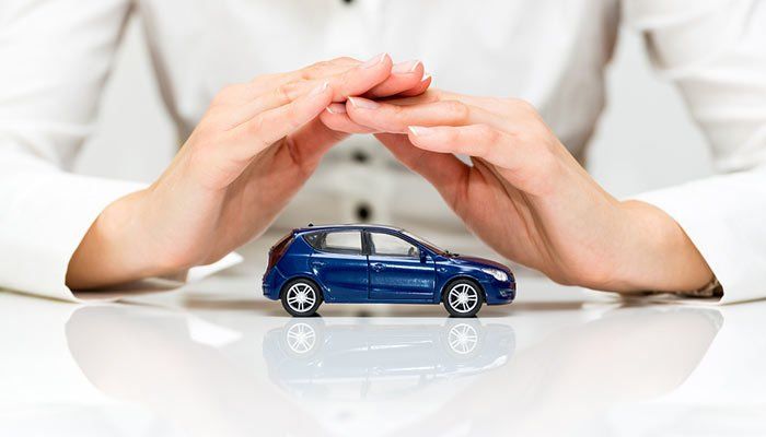 Unas manos protegen un coche de juguete azul sobre una superficie blanca.