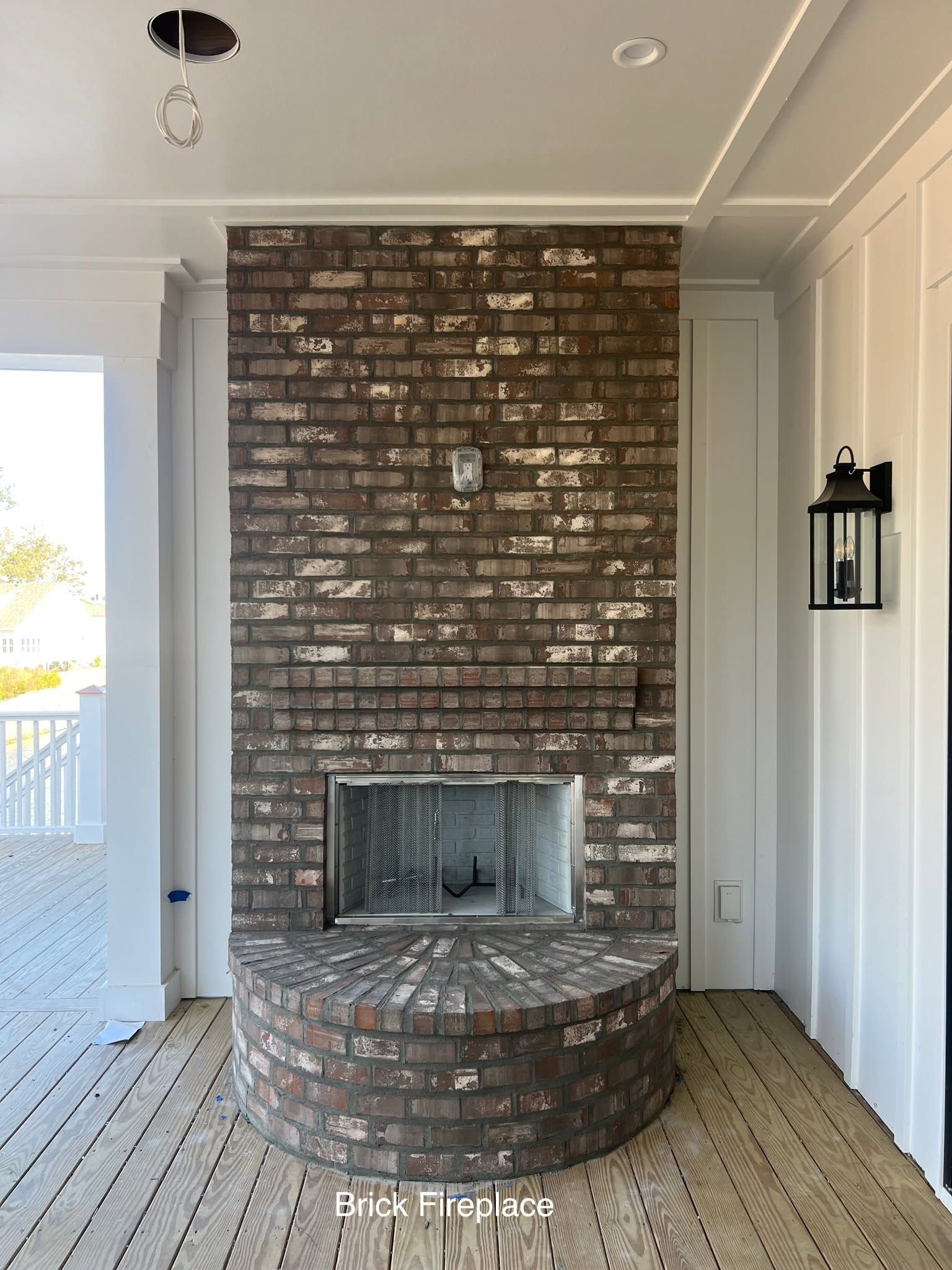 Brick outdoor fireplace on a covered porch with white siding and a curved brick hearth
