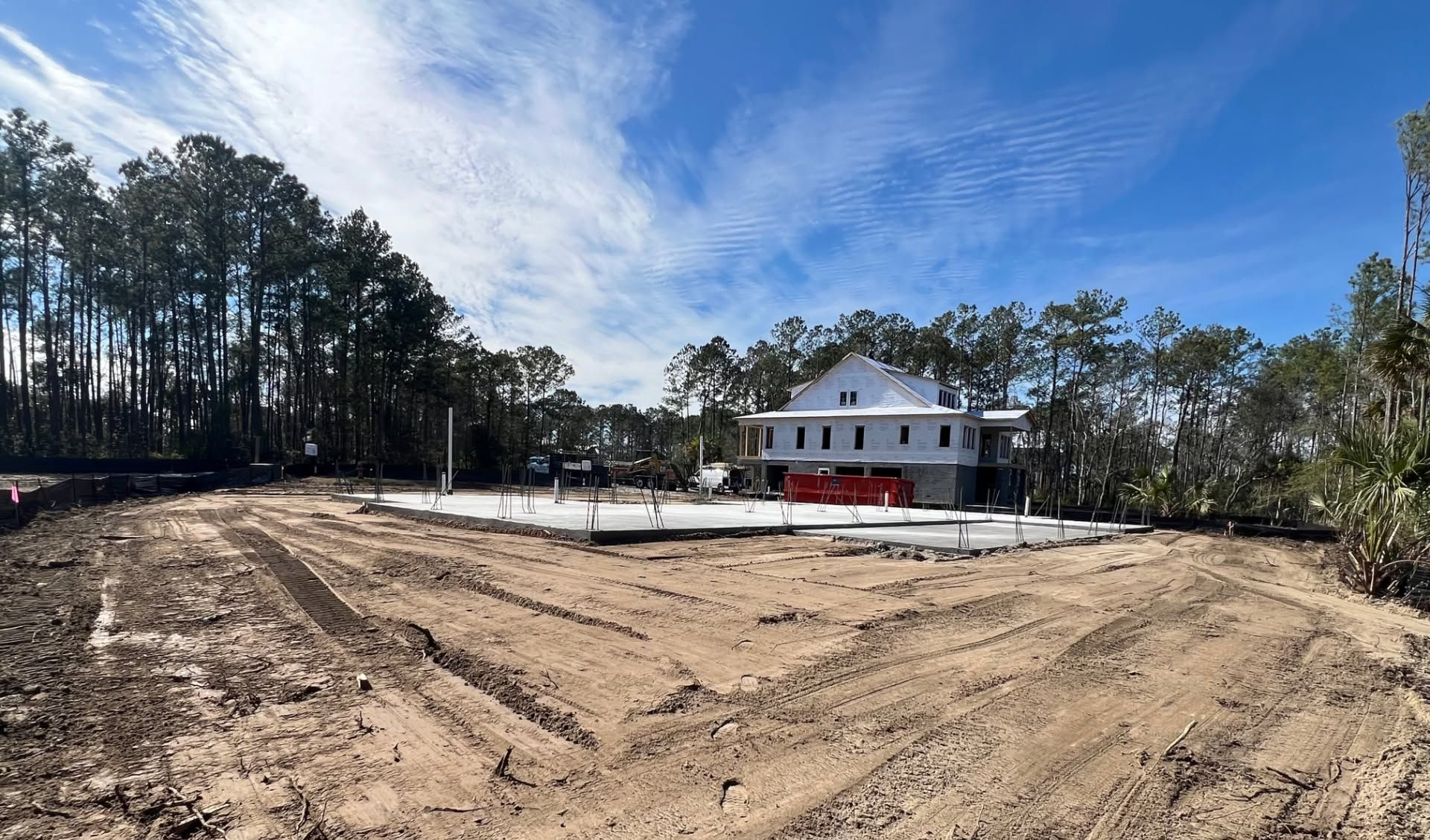 House under construction on a cleared lot with trees and blue sky in the background