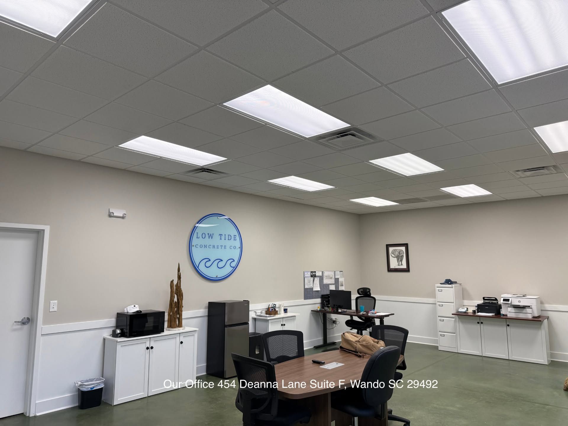 Office room with desks, cabinets, printer, and a blue wall clock under bright ceiling lights