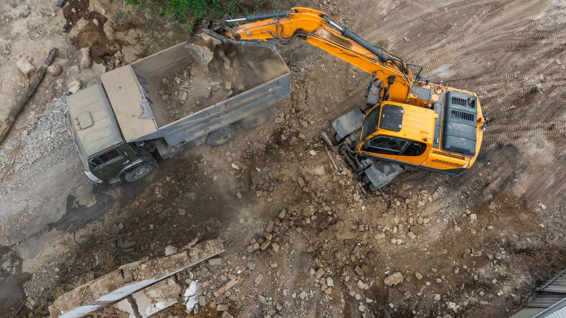 Orange excavator loading dirt into a dump truck at a muddy construction site