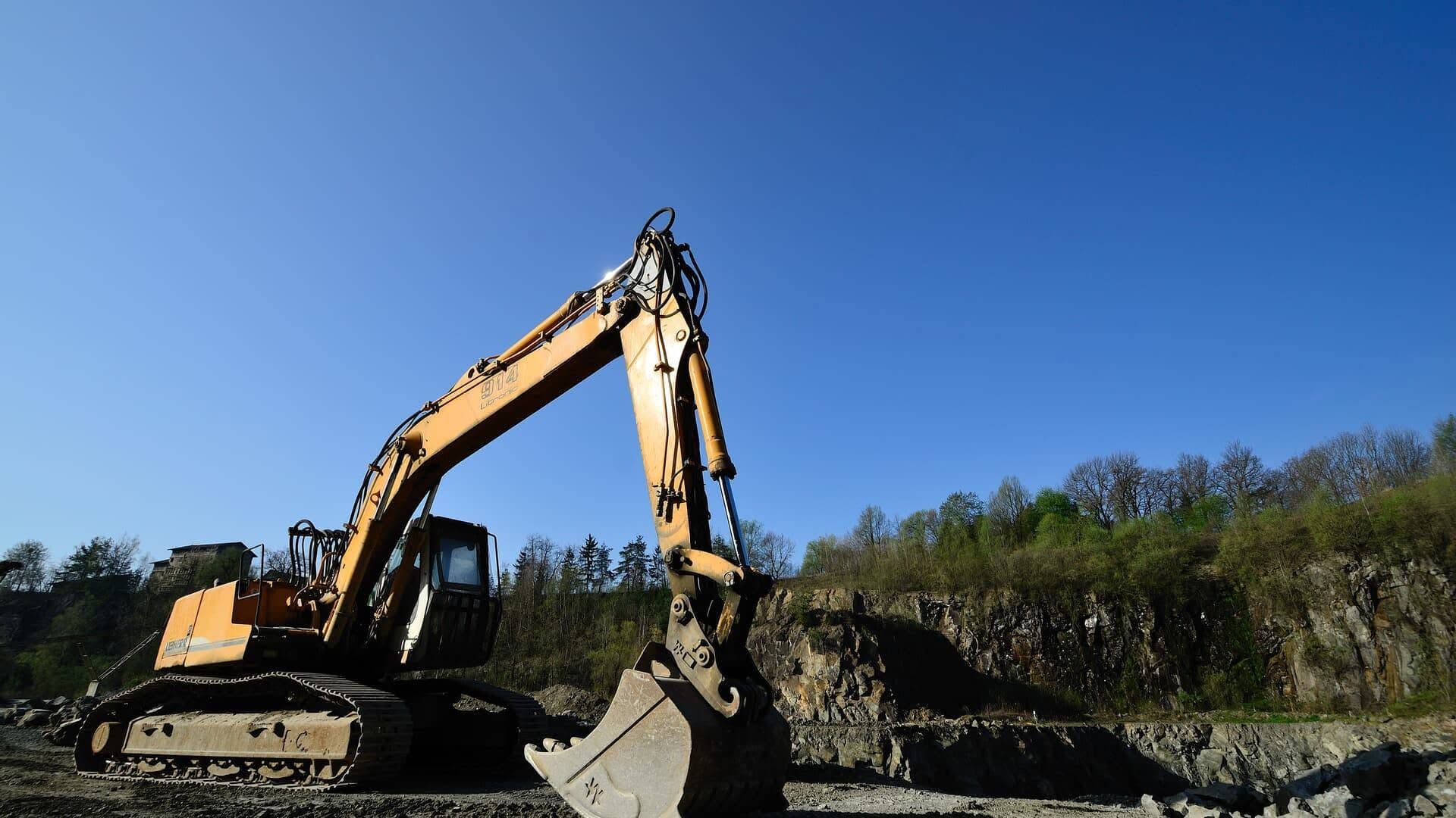 Yellow excavator digging dirt at a construction site under a clear blue sky