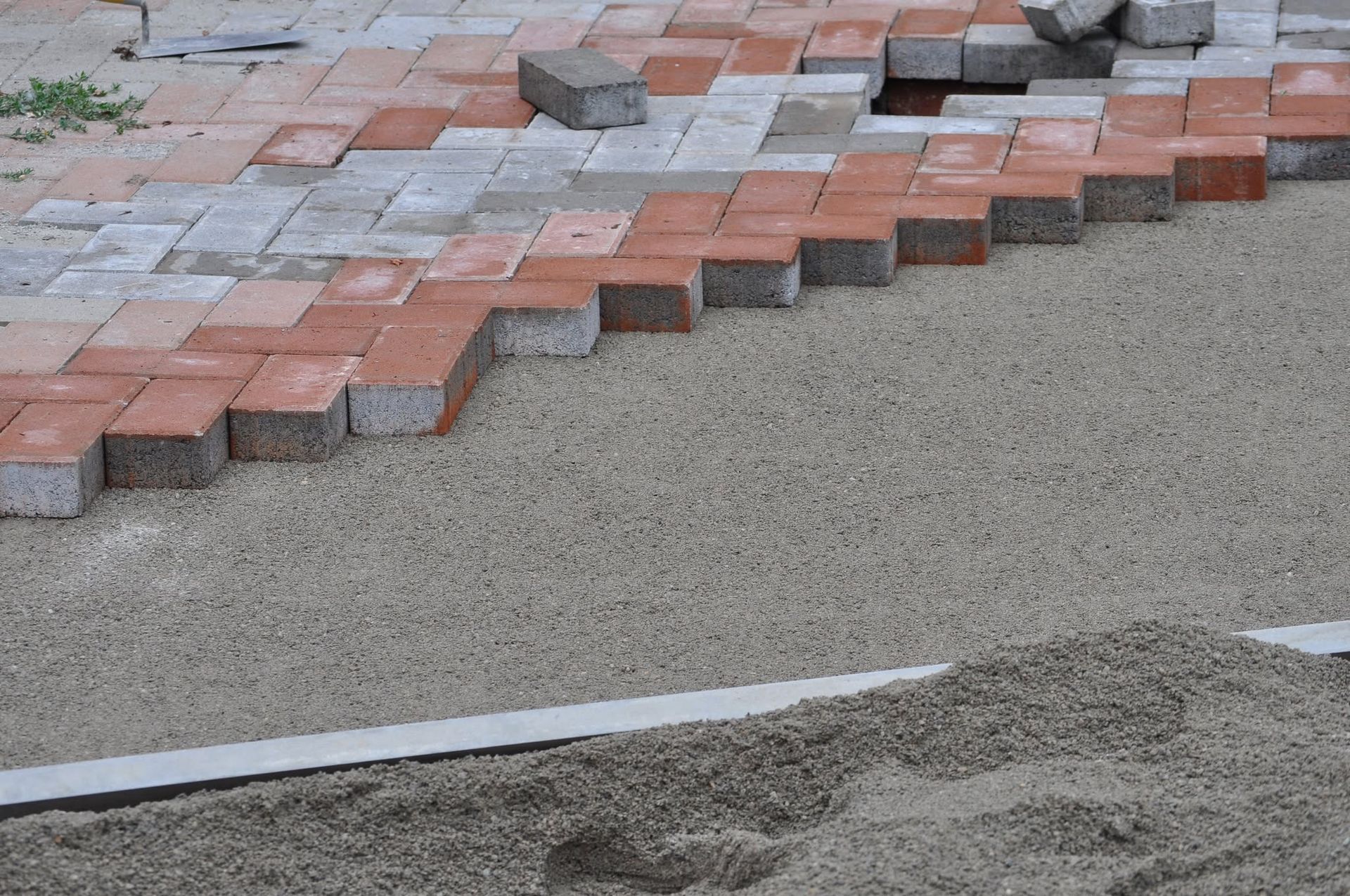 Red and gray paving stones forming a stepped edge beside a sand-covered work area