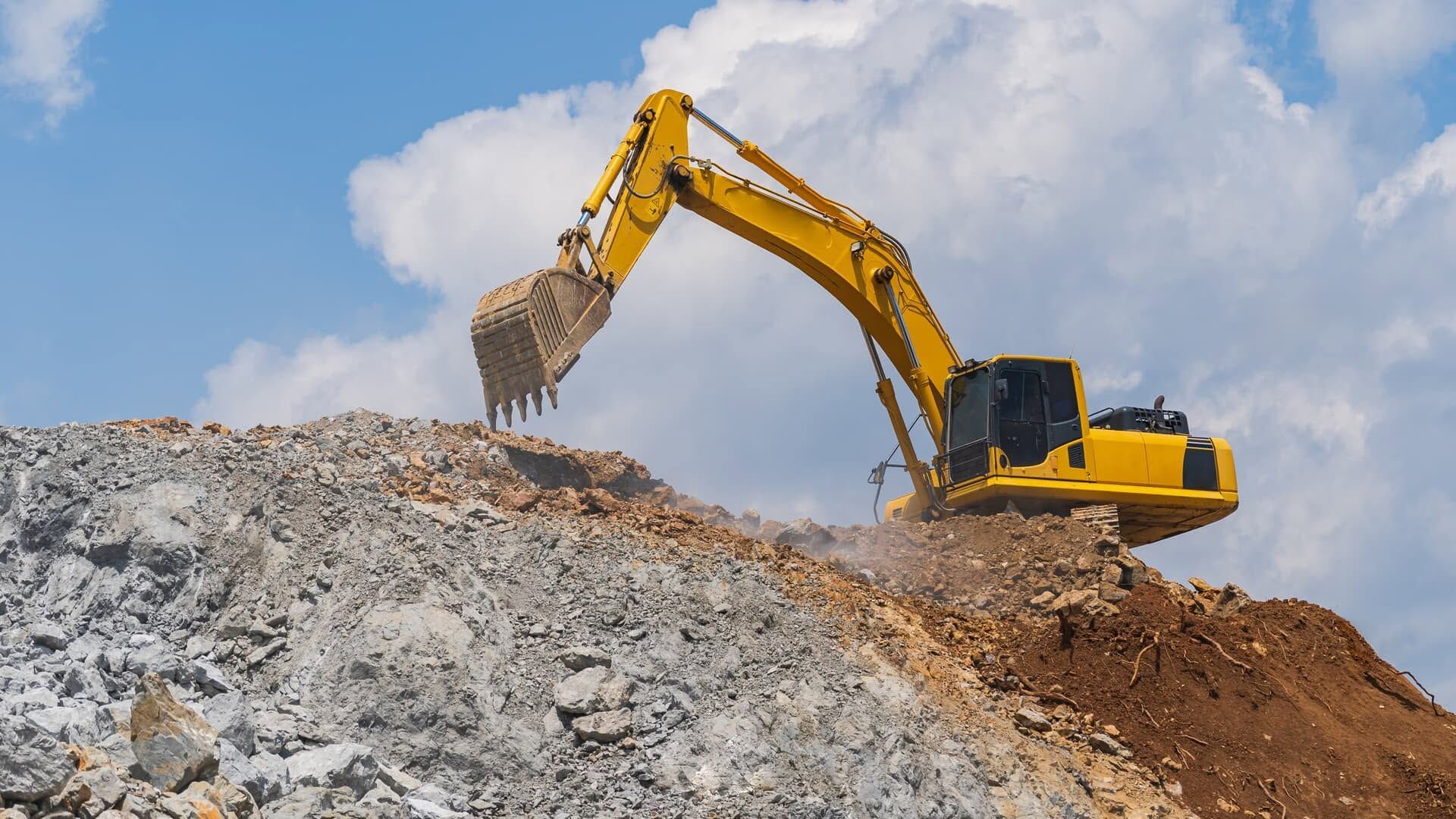 Yellow excavator digging earth on a rocky construction site under a cloudy sky