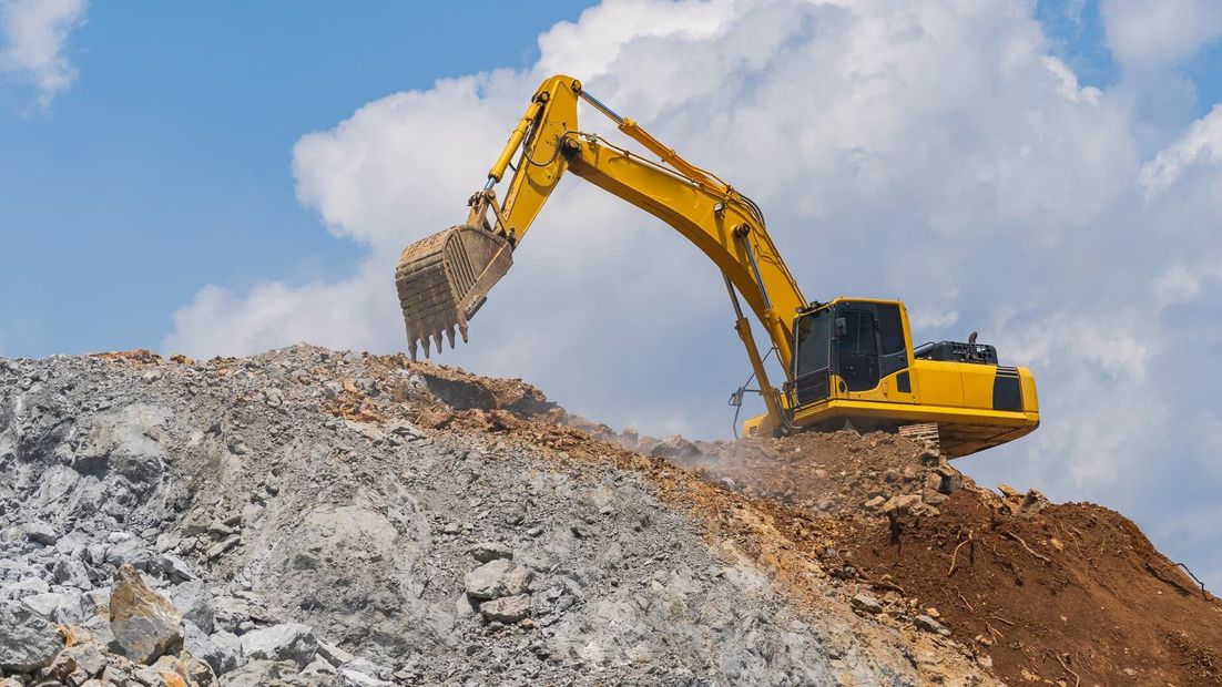 Yellow excavator digging into a gravel mound under a blue sky.