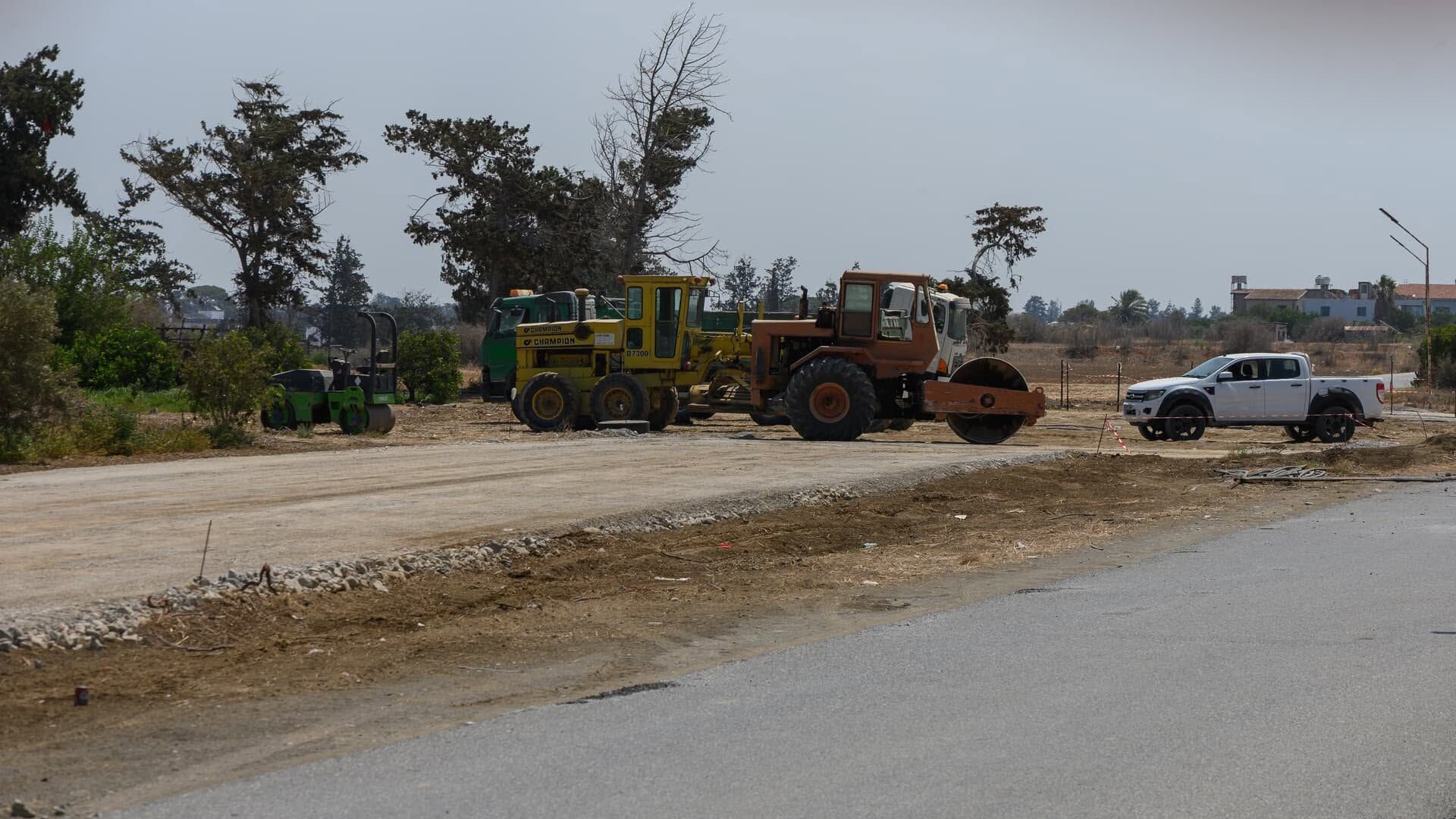 Roadwork scene with a backhoe, construction truck, and pickup on a dusty roadside
